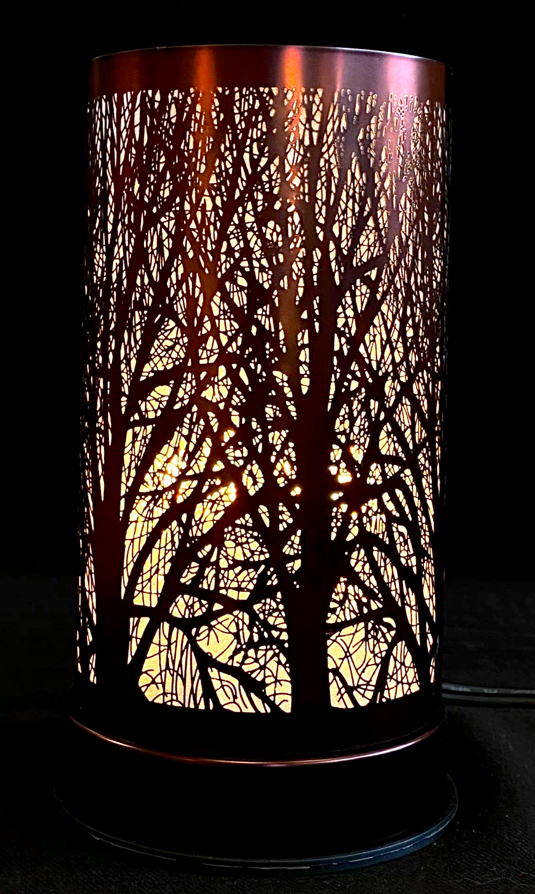 bronze coloured cylindrical lamp with trees on the side against a black background